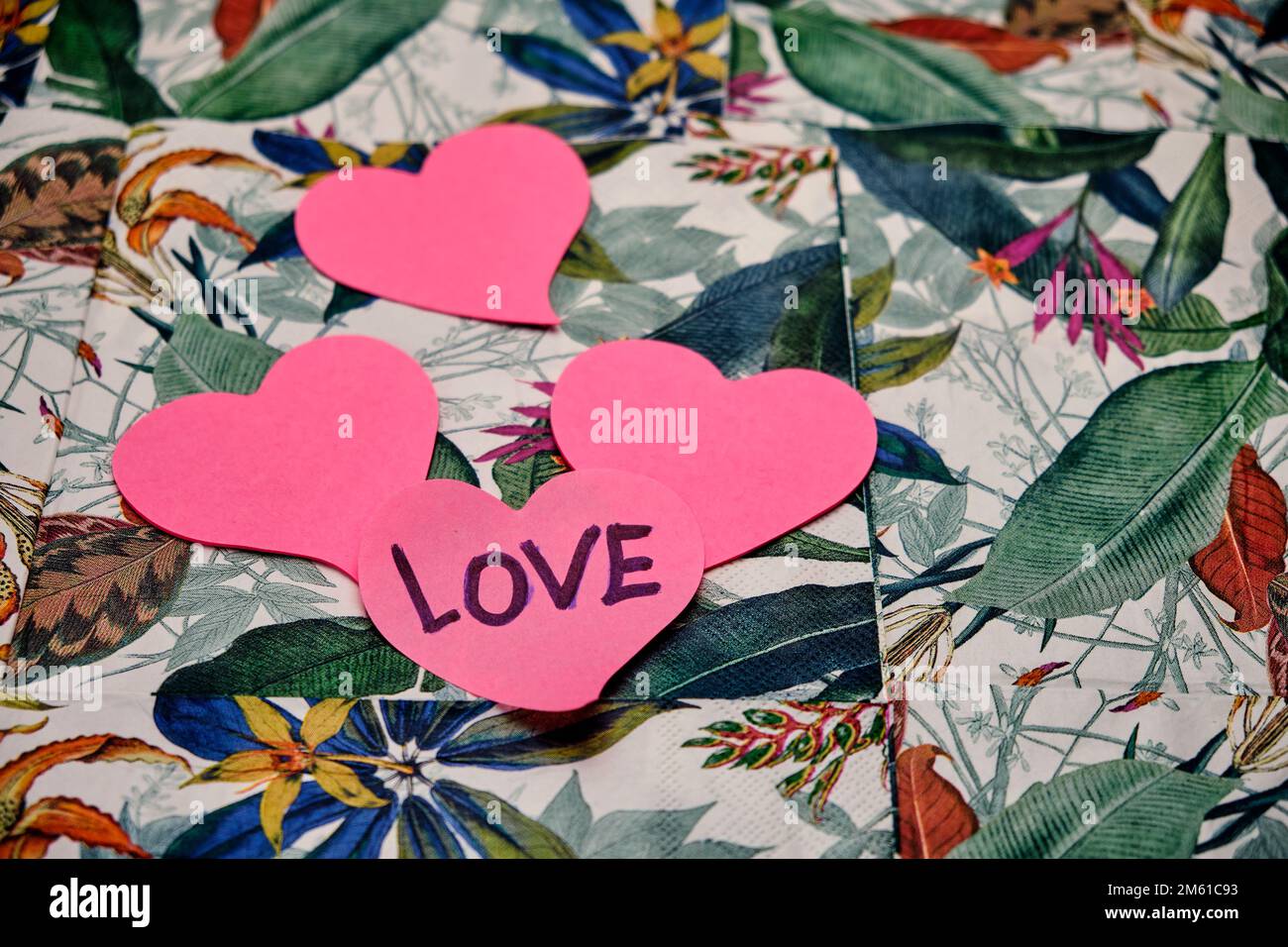 Quatre coeurs roses sur l'un d'eux ont écrit le mot amour, sur une table avec un motif tropical. Banque D'Images