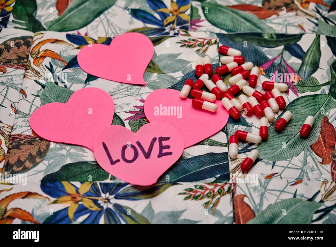 Quatre coeurs roses dans l'un d'eux ont écrit le mot amour avec beaucoup de pilules, sur une table avec un modèle tropical. Banque D'Images