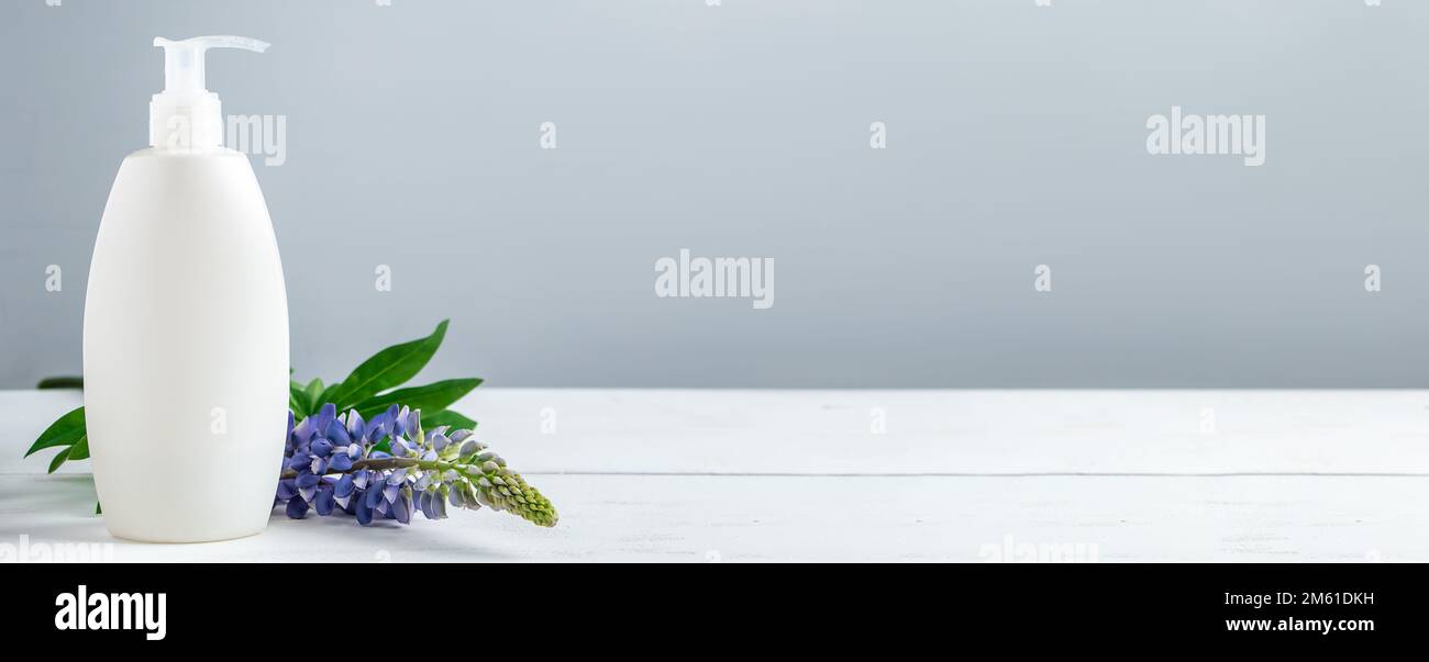 Bouteille cosmétique avec lotion et fleurs lupin sur fond gris. Cosmétiques naturels pour les soins du corps et du visage. Concept de produits spa bio, relaxati Banque D'Images