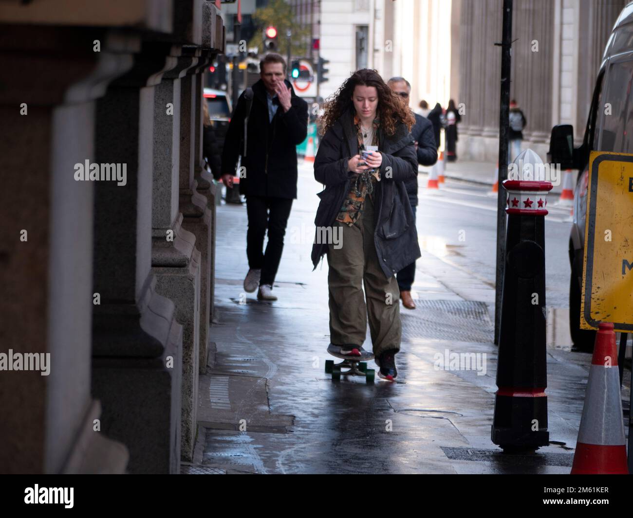 Femme skateboarder, patinage dans la rue Threadneedle regardant le téléphone Banque D'Images