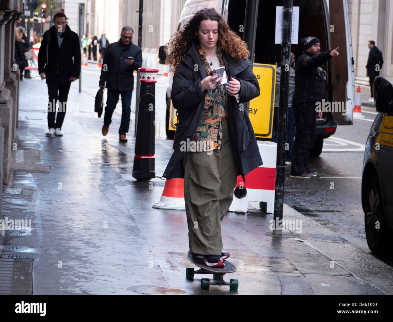 Femme skateboarder, patinage dans la rue Threadneedle regardant le téléphone Banque D'Images