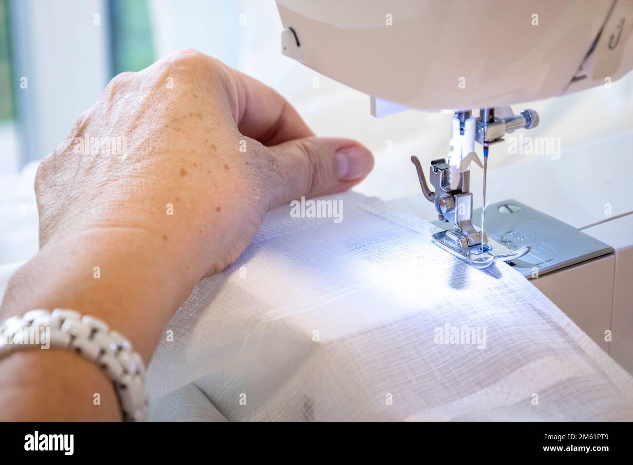 Vue rapprochée du dessus du tissu de couture des mains de femmes en machine de fabrication sur le lieu de travail. Pied de pression de l'aiguille avec fond blanc flou Banque D'Images