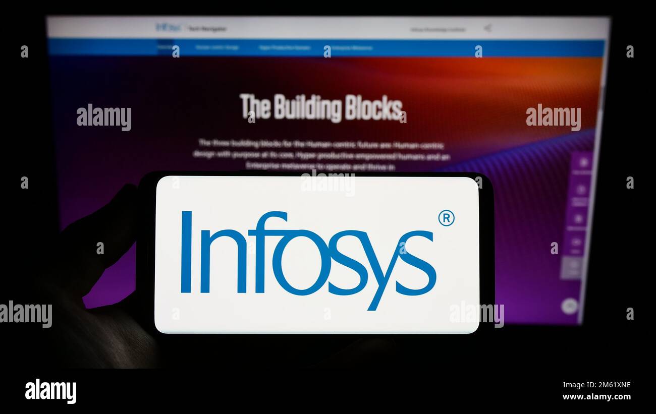 Personne tenant un smartphone avec le logo de la société indienne DE TI Infosys Limited à l'écran devant le site Web. Mise au point sur l'affichage du téléphone. Banque D'Images