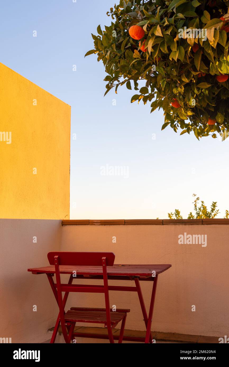 Table et chaises en bois rouge sous un arbre orange sur la terrasse d'une maison au coucher du soleil Banque D'Images