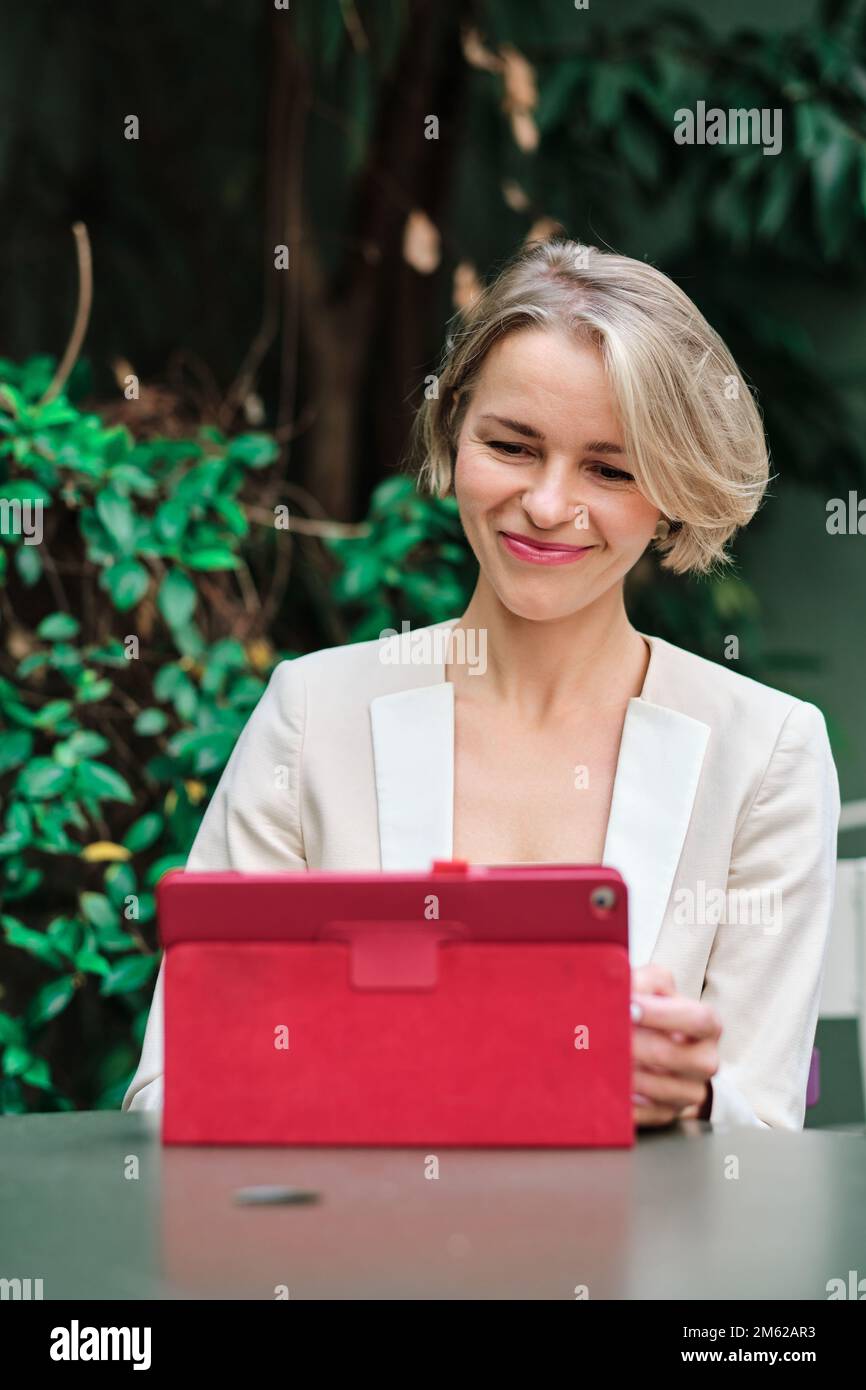 Femme souriant en utilisant une tablette numérique assis sur une table à l'extérieur. Banque D'Images