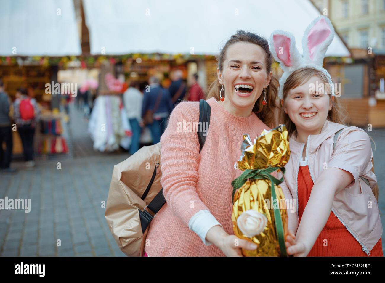 Pâques amusant. Portrait de la jeune mère et de l'enfant souriants avec un œuf de pâques doré à la foire de la ville. Banque D'Images