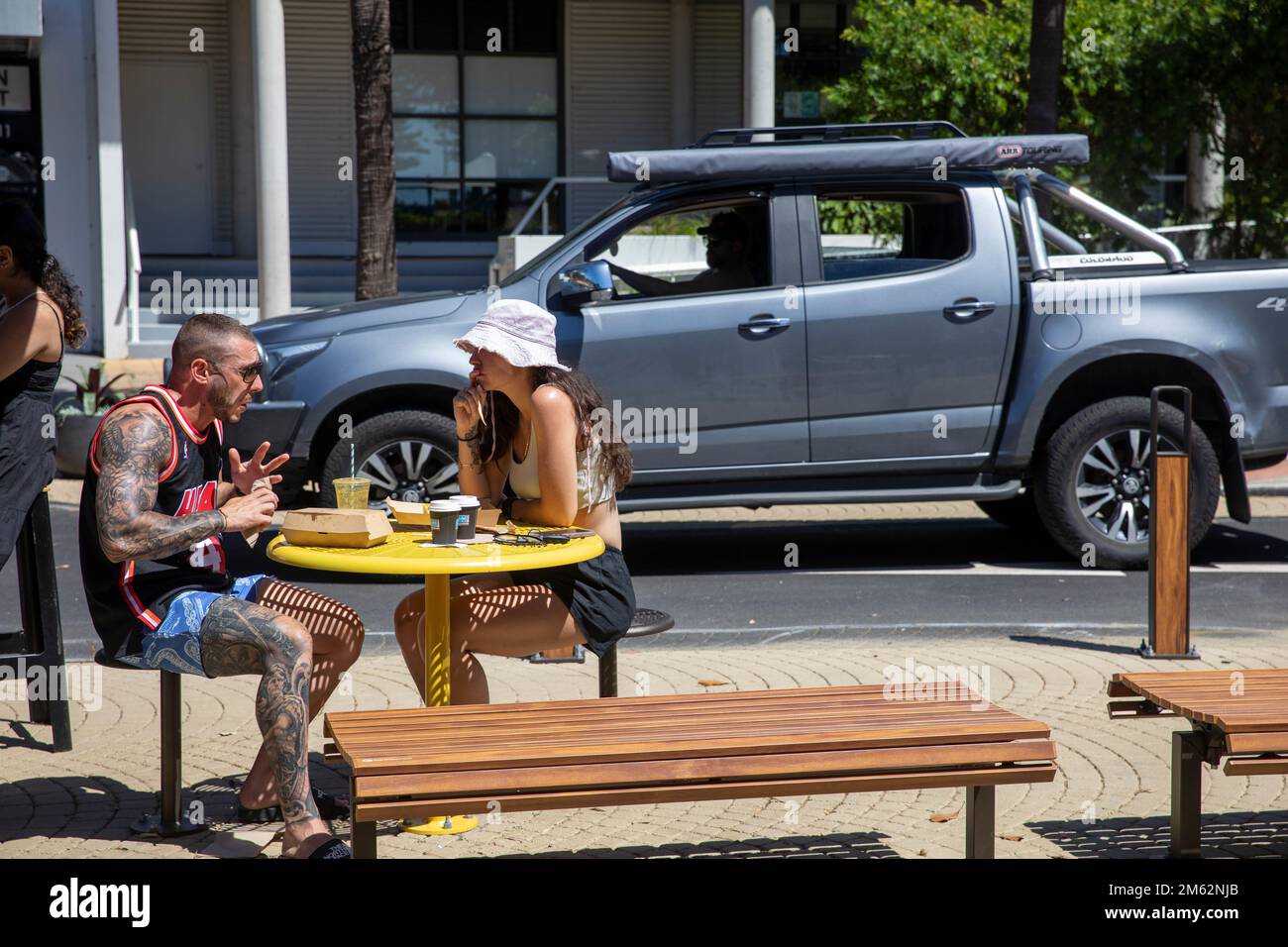 Couple dehors ayant un café à Avalon Beach café, l'homme est fortement tatoué sur le bras droit et la jambe, jeune femme n'a pas de tatouages, Sydney, NSW, Australie Banque D'Images