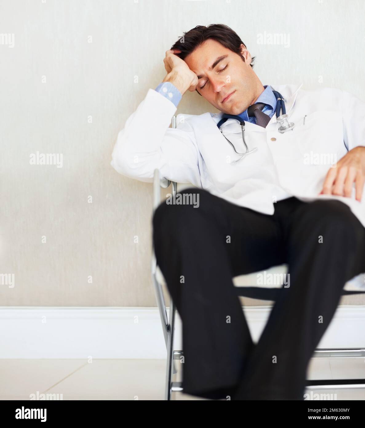 Jeune médecin fatigué dormant sur une chaise à l'hôpital. Portrait d'un jeune médecin fatigué dormant sur une chaise à l'hôpital. Banque D'Images