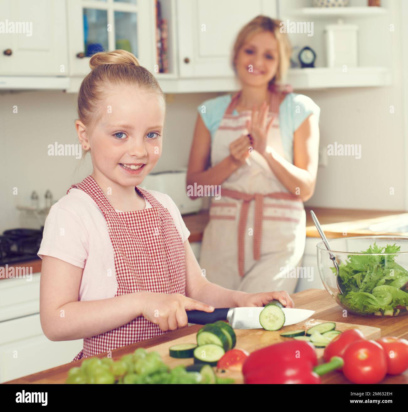 Aider sa mère à faire le déjeuner. Une petite fille faisant une salade dans la cuisine avec sa mère debout à proximité. Banque D'Images
