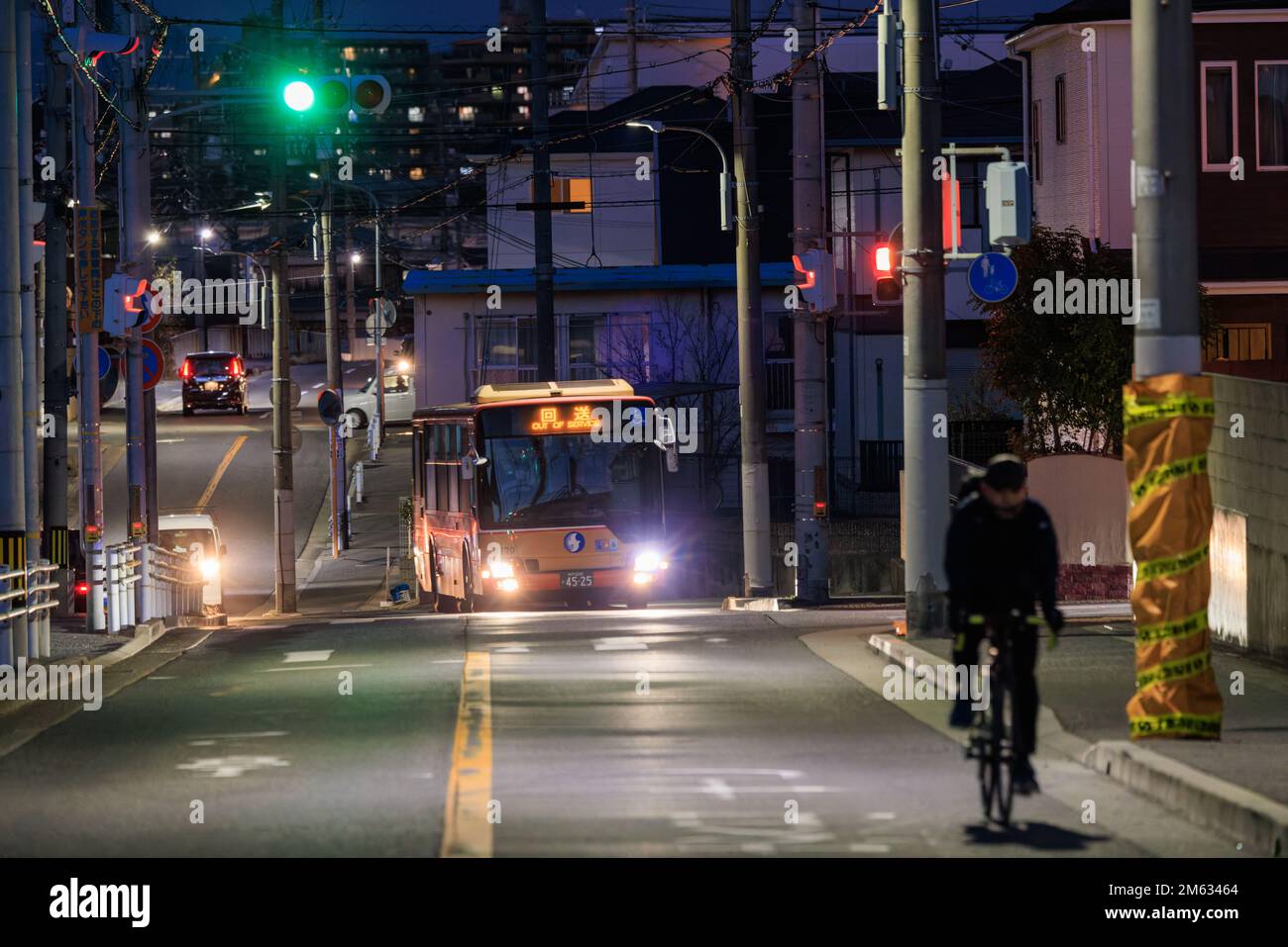 Akashi, Japon - 29 décembre 2022: Le cycliste passe sur la route de banlieue à l'approche du bus la nuit Banque D'Images