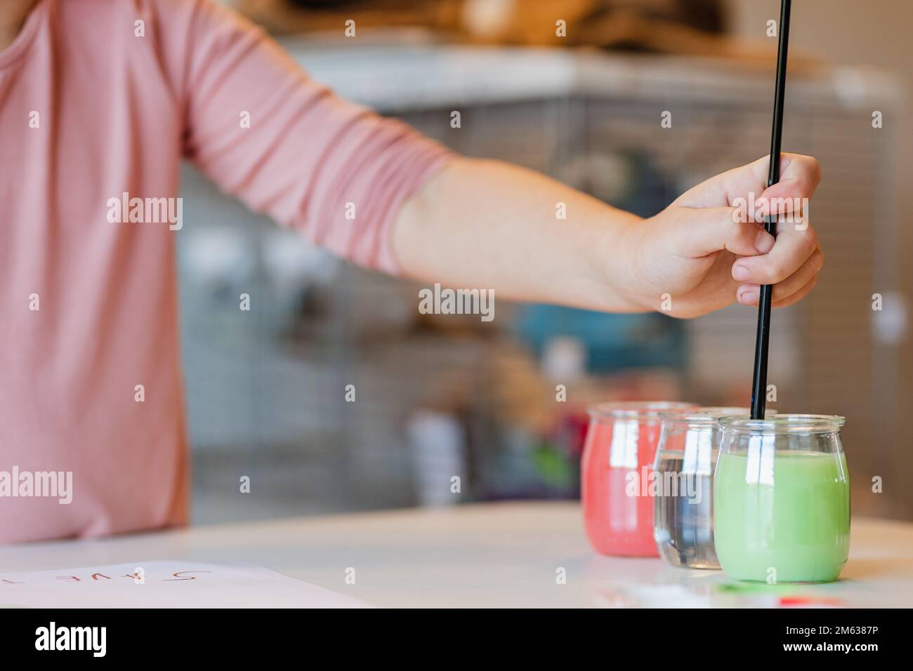 Un enfant méconnaissable se concentre sur des vêtements décontractés, laver la peinture au pinceau dans une tasse avec de l'eau tout en peignant l'image pendant la leçon d'art à l'école Banque D'Images