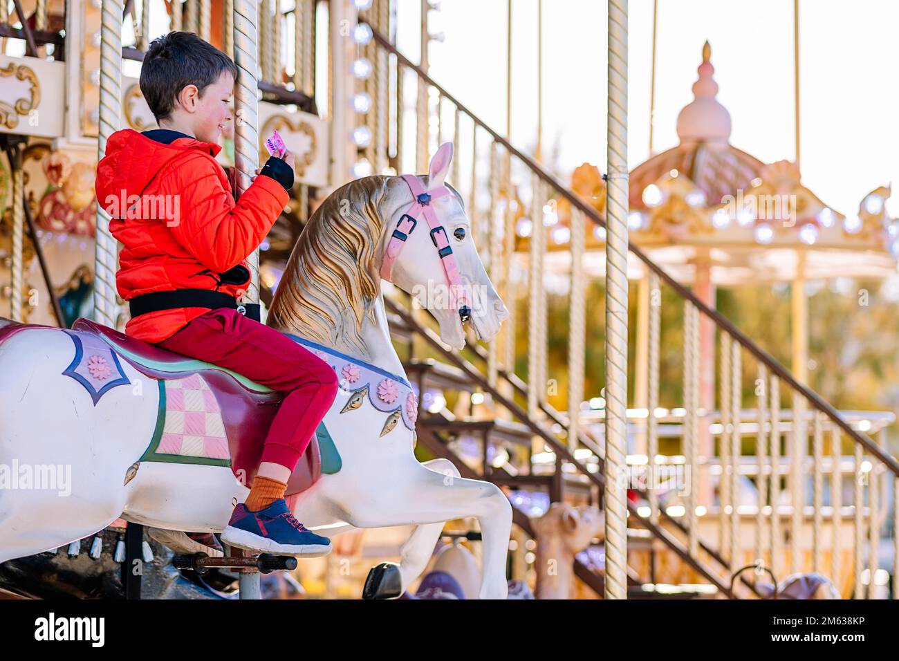 Plein corps Happy boy en vêtements d'extérieur souriant et assis à cheval tout en faisant du carrousel le jour ensoleillé sur le champ de foire de Donostia San Sebastian, Espagne Banque D'Images