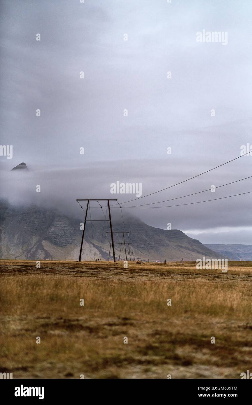 Paysage paisible avec un champ herbacé sec près de la montagne rocheuse avec des pics pointus cachés sous les nuages gris en Islande Banque D'Images