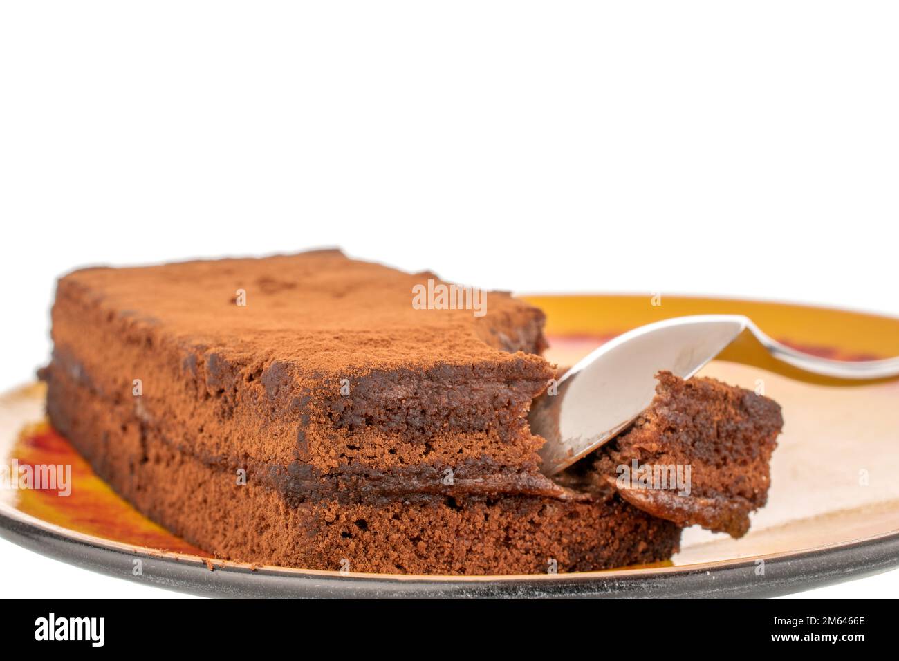 Un morceau de gâteau à la truffe sur une soucoupe en céramique avec une cuillère en métal, macro, isolée sur fond blanc. Banque D'Images