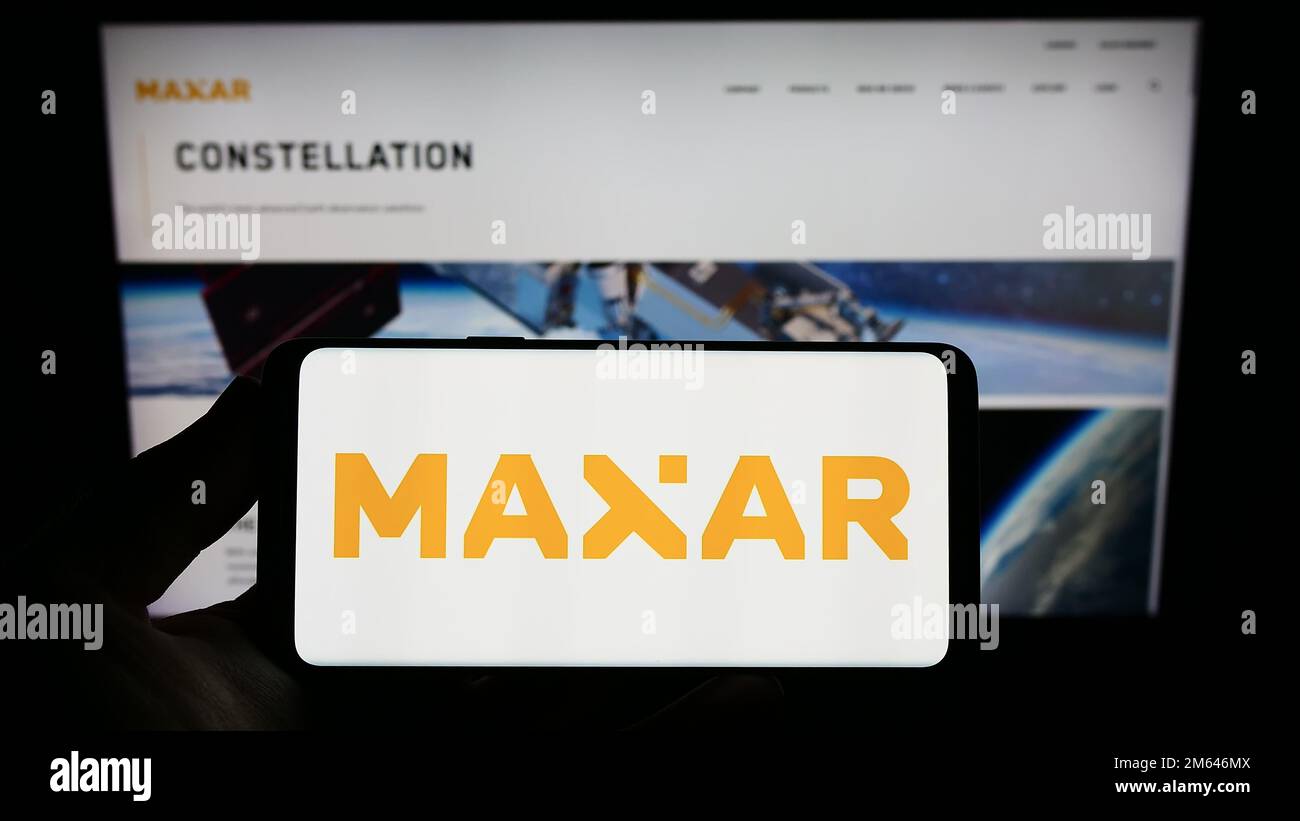 Personne tenant un smartphone avec le logo de la société spatiale américaine Maxar technologies Inc. À l'écran devant le site Web. Mise au point sur l'affichage du téléphone. Banque D'Images