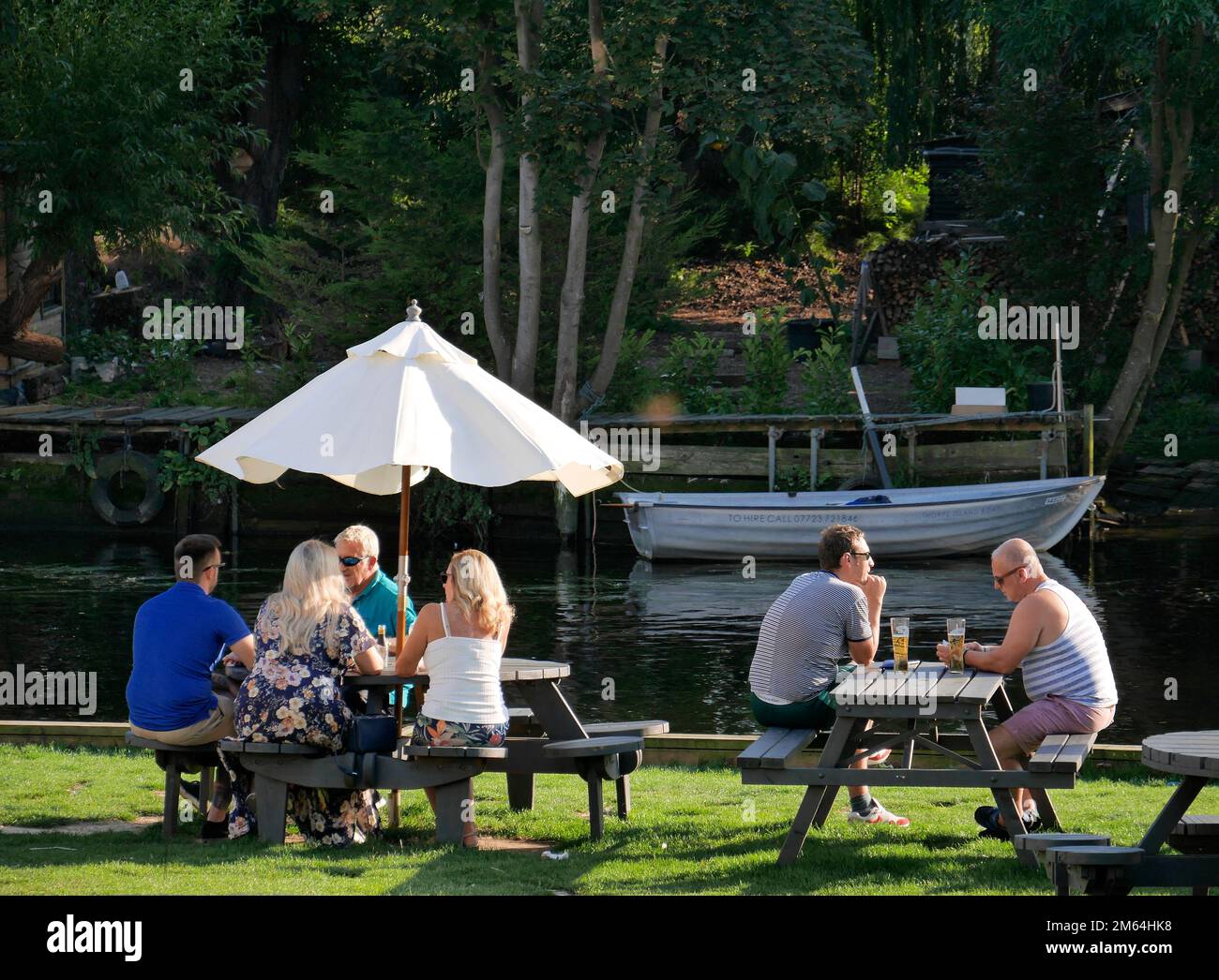 Groupes de personnes assis dehors sur des bancs de pique-nique à Riverside Pub Garden, Thorpe St Andrew, Norwich, Norfolk, Angleterre, ROYAUME-UNI Banque D'Images