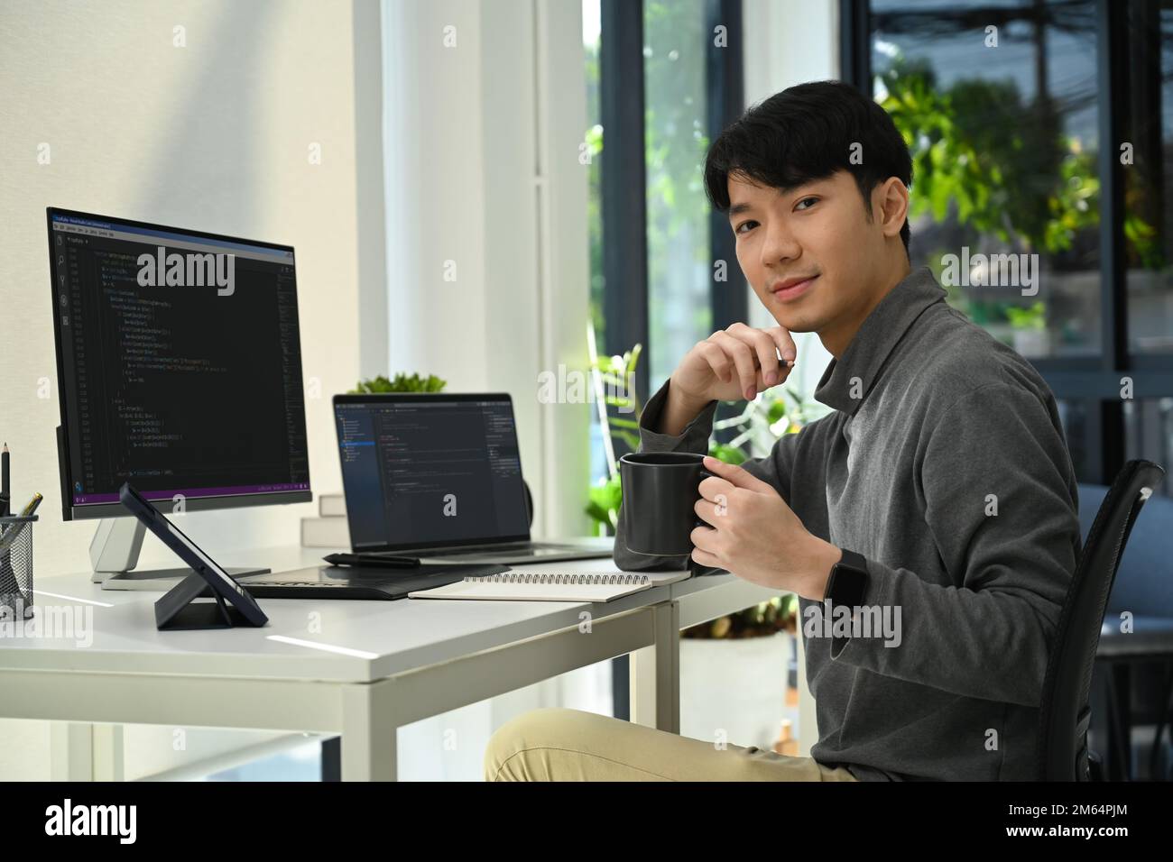 Jeune programmeur asiatique masculin assis à son poste de travail avec des données codées sur un ordinateur de bureau Banque D'Images