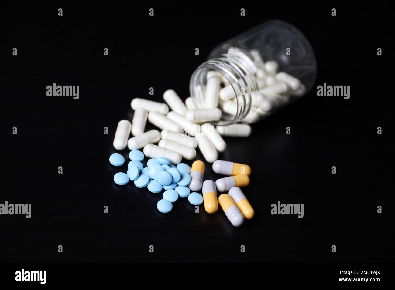 Différentes pilules sur une table en bois noir, variation des médicaments dans les capsules dispersées d'une bouteille. Contexte pour la pharmacie, les antibiotiques, les vitamines Banque D'Images