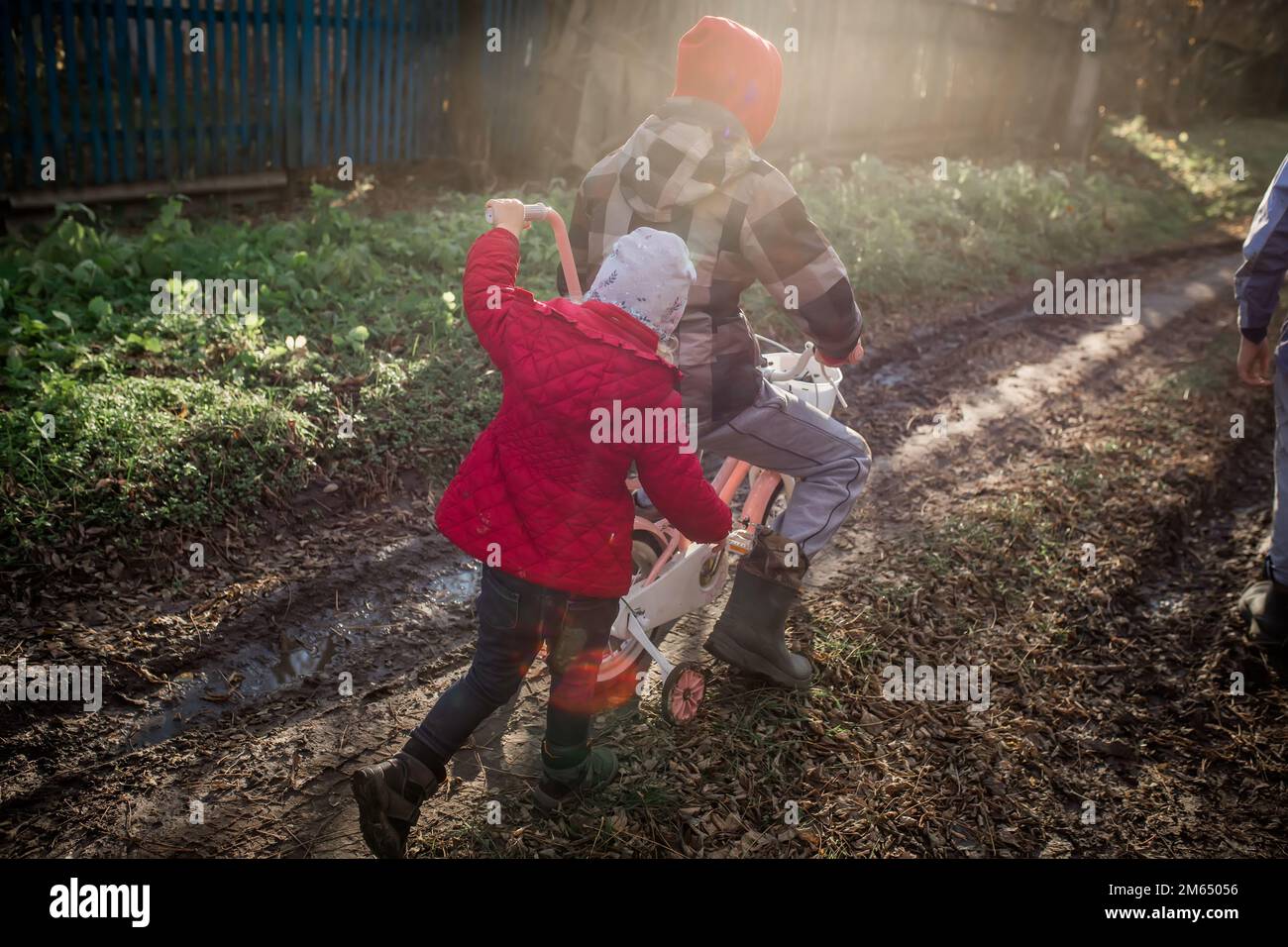 Une fille pousse un vélo avec son frère aîné. Les enfants d'immigrants s'amusent dans le village. Un village isolé sans routes. Enfant ukrainien mov Banque D'Images