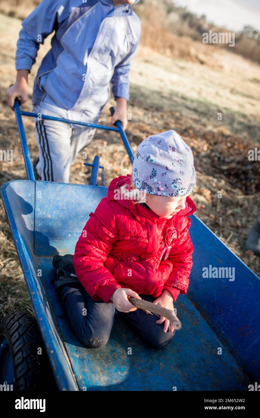 Une petite fille dans un chariot de jardin bleu. Frère et sœur s'amusent tout en préparant le jardin Banque D'Images