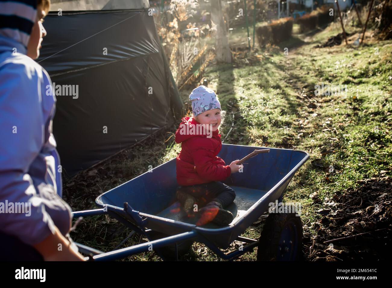 Une petite fille dans un chariot de jardin bleu. Frère et sœur s'amusent tout en préparant le jardin Banque D'Images