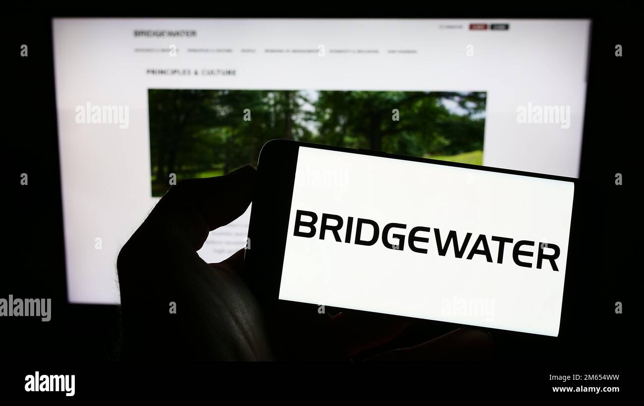 Personne tenant un téléphone mobile avec le logo de la société d'investissement américaine Bridgewater Associates LP à l'écran en face de la page Web. Mise au point sur l'affichage du téléphone. Banque D'Images