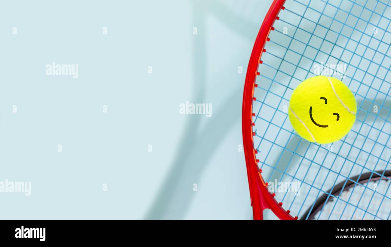 Bannière de compétition de tennis. Composition sportive avec ballon de tennis jaune avec visage de sourire et raquettes de tennis sur fond bleu avec espace de copie. Sport an Banque D'Images