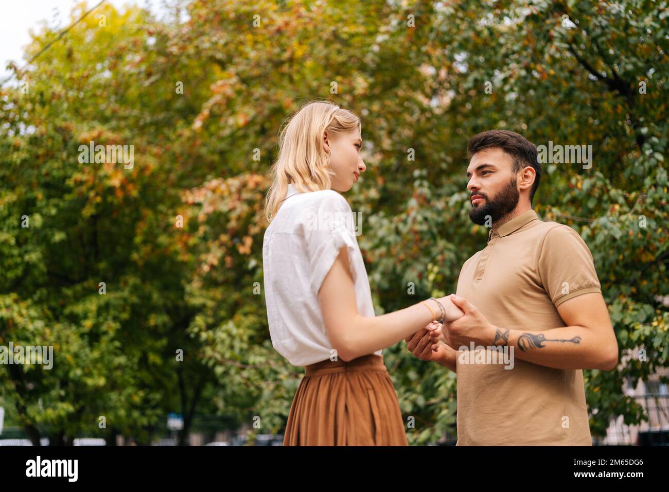 Prise de vue de dessous de joli jeune couple amoureux debout dans le parc de la ville et regardant les uns les autres avec des yeux tombant amoureux. Banque D'Images