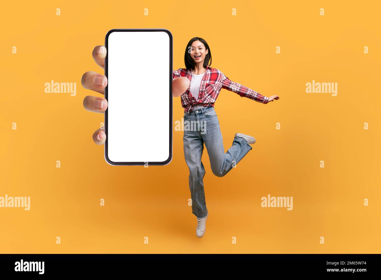 Pleine longueur de femme asiatique heureuse sauter et montrant le téléphone portable avec espace vide pour l'application mobile ou le site Web, maquette Banque D'Images