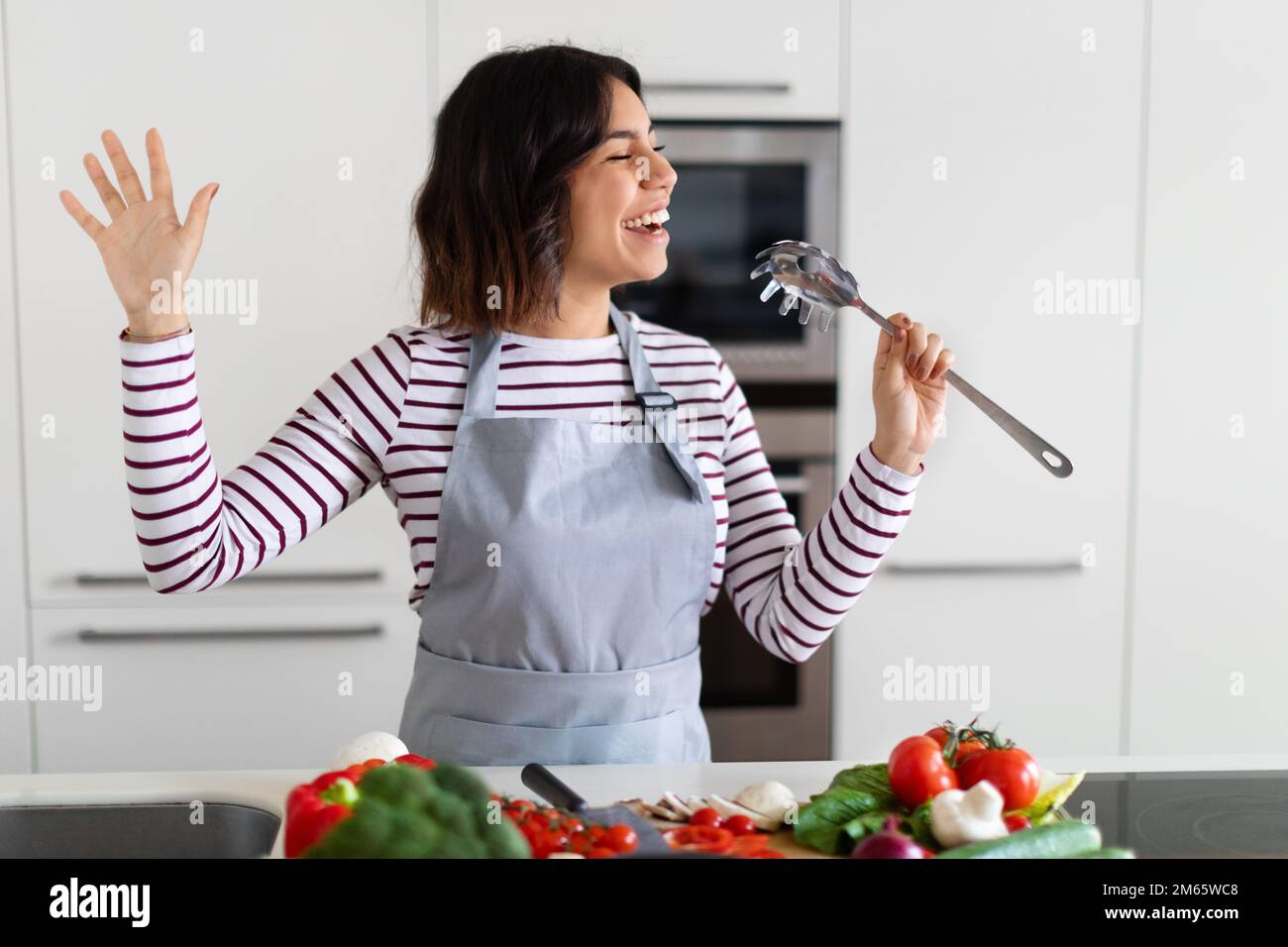Joyeuse femme heureuse chantant tout en cuisinant dans la cuisine Banque D'Images