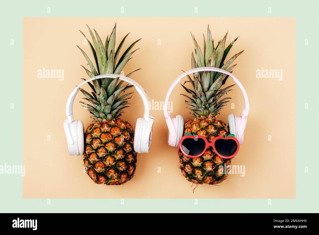Deux ananas en lunettes de soleil avec écouteurs sur fond vert clair et jaune. Concept d'été. Vue de dessus, plan d'agencement. Banque D'Images