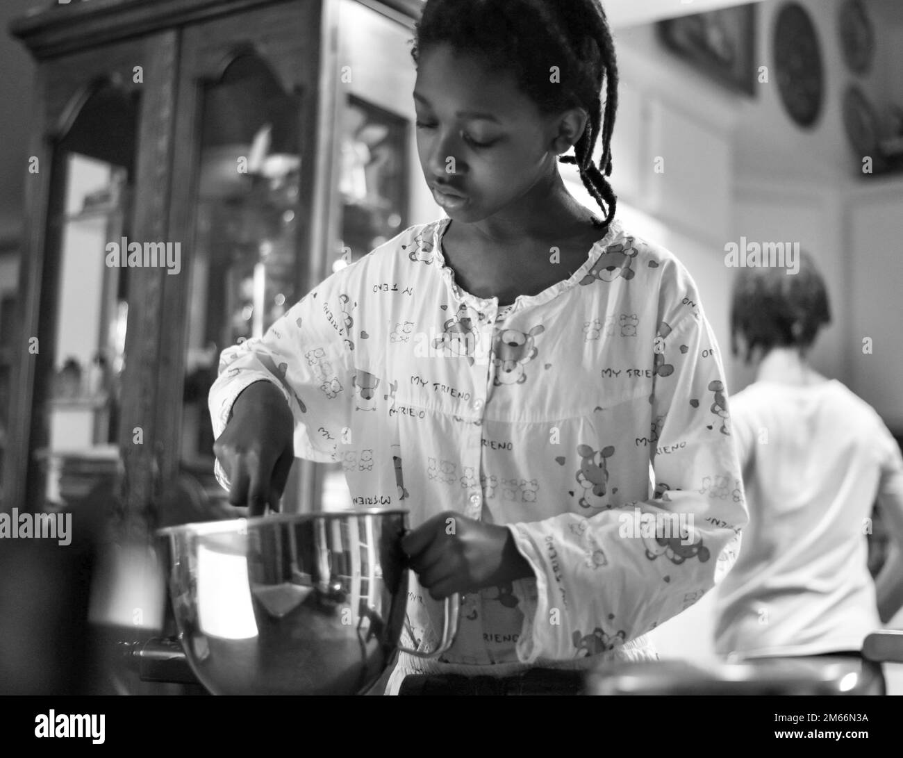 photo en noir et blanc d'une jeune fille mélangeant les ingrédients du petit déjeuner dans un bol en acier inoxydable brillant Banque D'Images