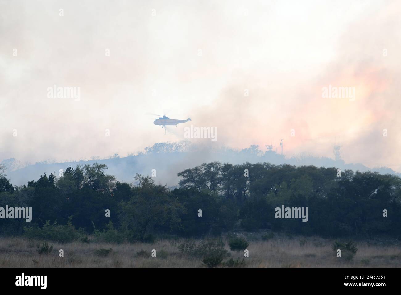 Un hélicoptère libère de l'eau sur un grand feu de forêt, le 9 avril 2022, à la zone de démolition de la base commune de San Antonio - Camp Bullis. JBSA-Camp Bullis comprend plus de 27 000 hectares de champs de tir, de zones d’entraînement et de terres sauvages du côté nord de San Antonio et est un lieu d’entraînement crucial pour les membres de la base conjointe de San Antonio. Banque D'Images