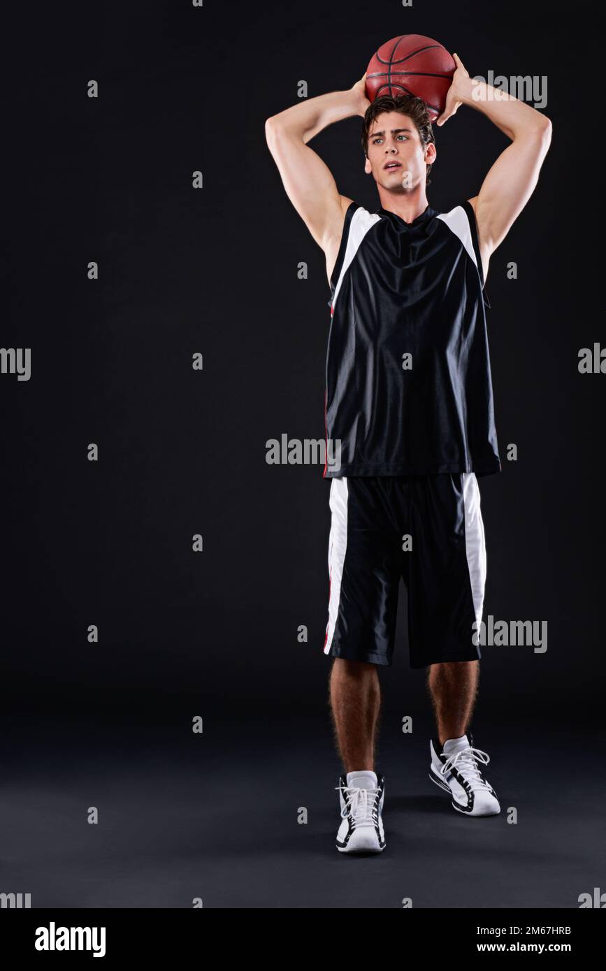 Il est temps de tirer quelques paniers. Prise de vue en studio d'un joueur de basket-ball masculin prêt à prendre une photo sur fond noir. Banque D'Images