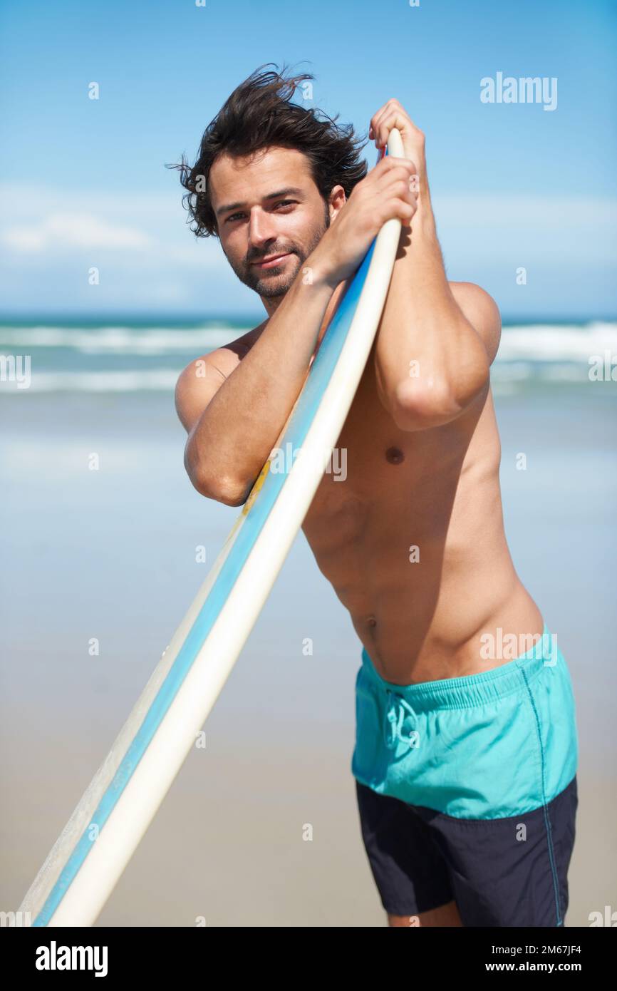 HES prêt à surfer. Un jeune homme s'est penché sur sa planche de surf à la plage. Banque D'Images