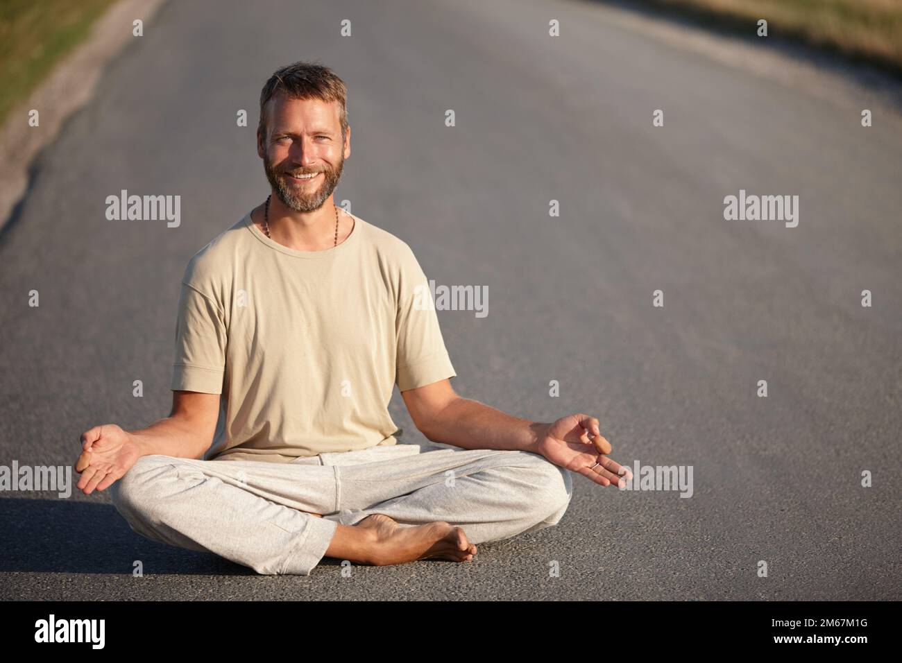 Le chemin du bonheur. Portrait d'un beau homme mûr assis dans la position lotus sur une route. Banque D'Images