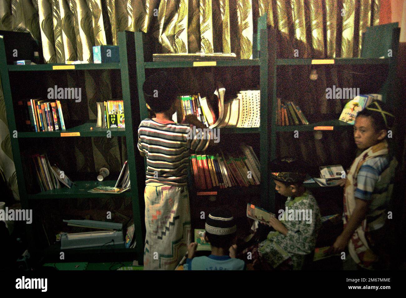 Les enfants ramassant des livres de la bibliothèque pour lire comme ils passent du temps dans une bibliothèque communautaire construite à l'intérieur d'une maison qui est utilisée comme camp de base du projet de reboisement dans le village de Sarongge à Ciputri, Pacet, Cipanas, West Java, Indonésie. Banque D'Images