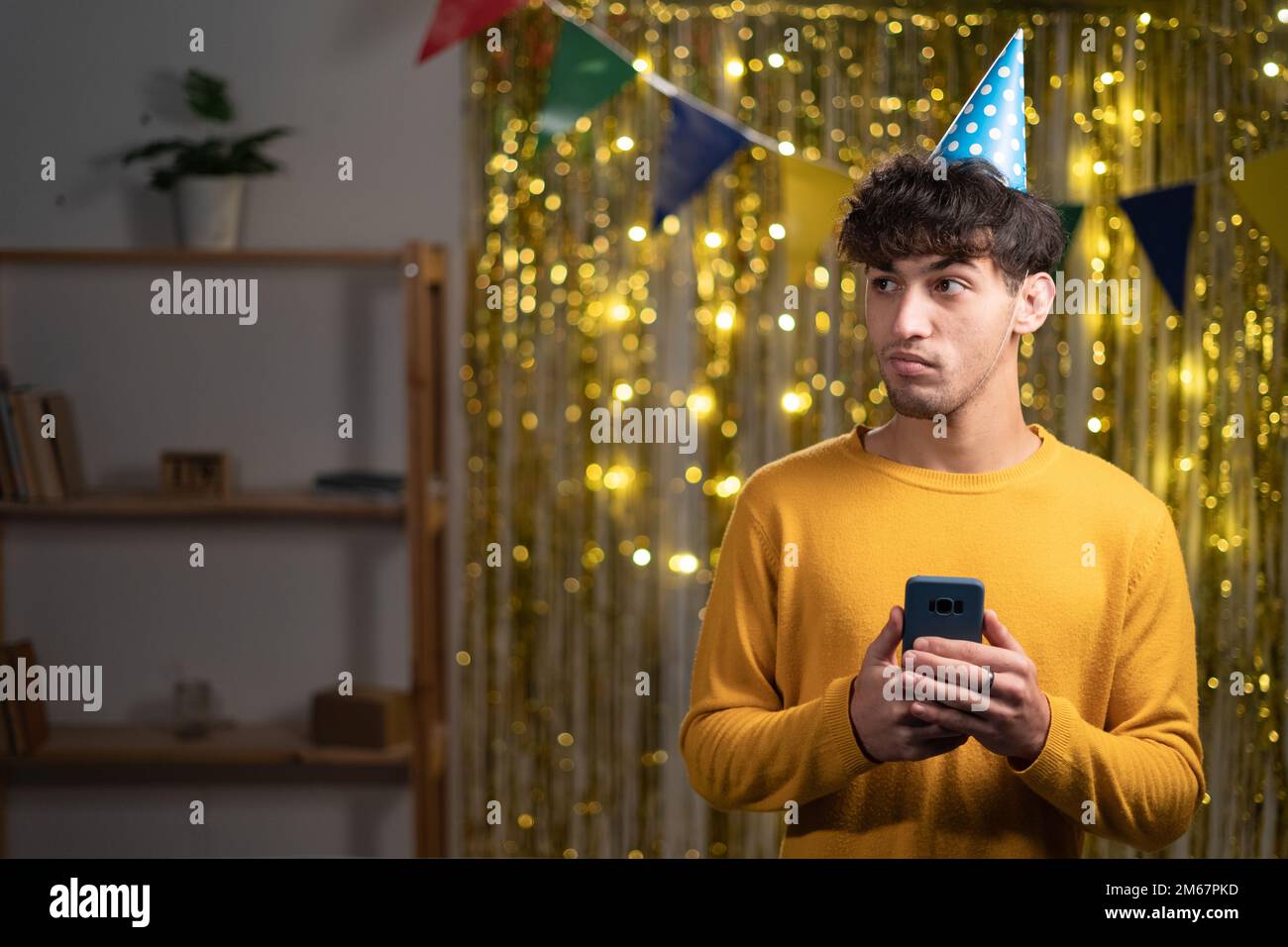 Portrait de charmant mec de ruse dans le chapeau de fête utiliser smartphone look bon plan d'espace d'imitation commentaire célébré anniversaire à la maison fête d'anniversaire. Banque D'Images