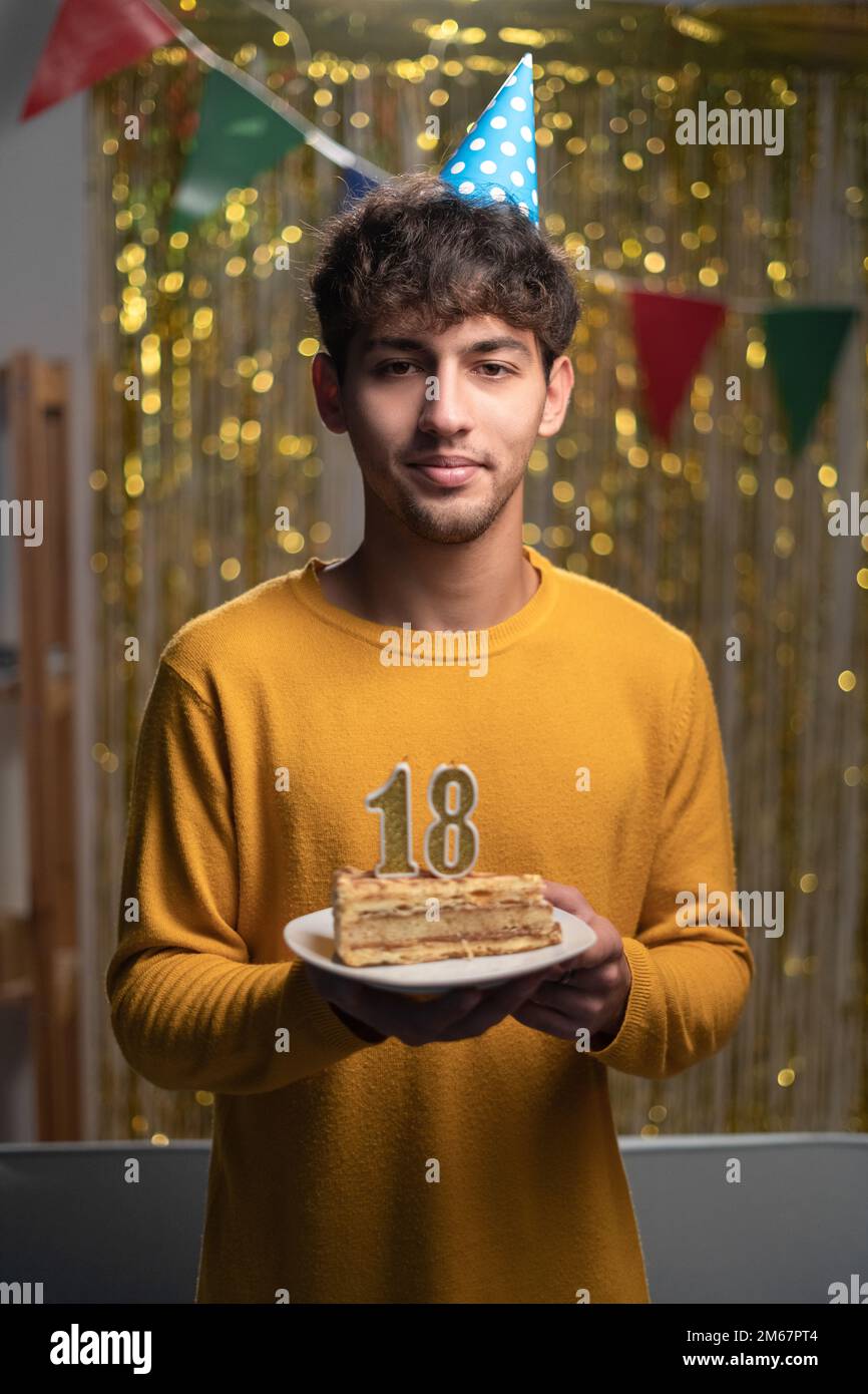 18th anniversaire. Jeune homme arabe en chapeau de fête tenant un gâteau avec le numéro 18 bougies célébrant l'anniversaire à la maison regardant l'appareil photo Banque D'Images