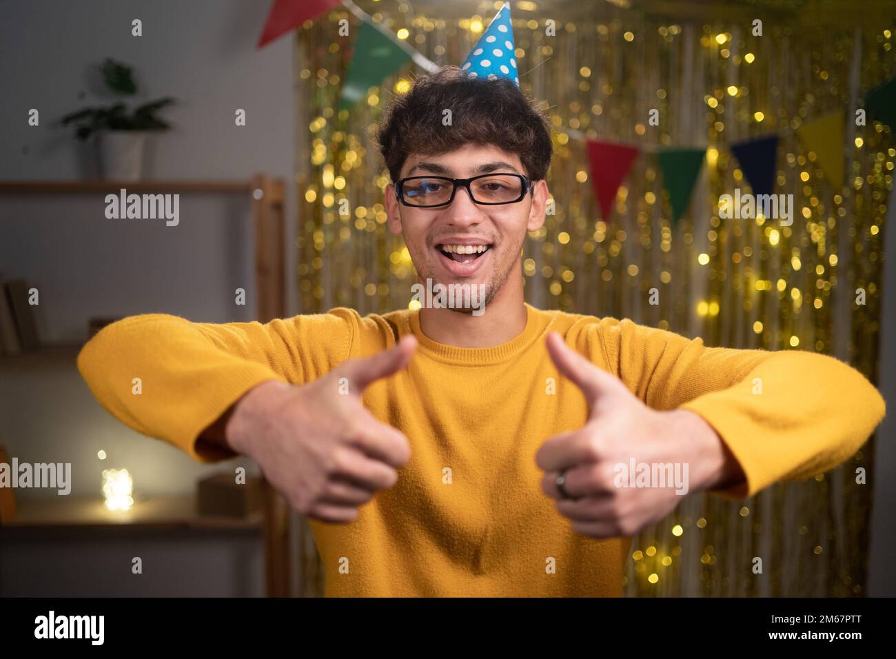 Homme arabe souriant célébrant l'anniversaire à la maison pouces vers le haut heureux avec la fête debout regardant l'appareil photo Banque D'Images