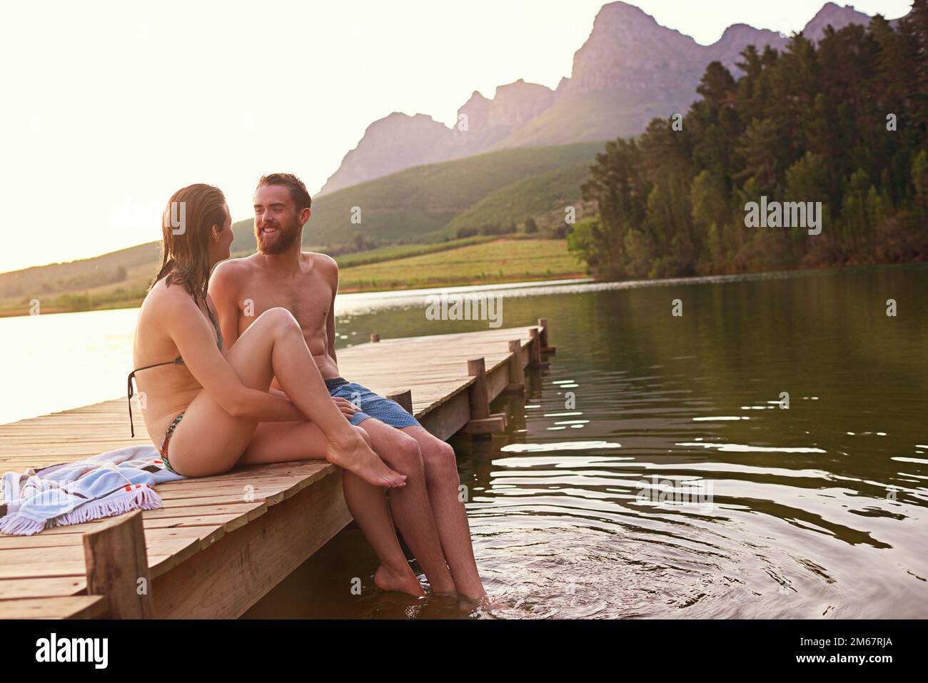 Été idyllique. un jeune couple affectueux en maillots de bain assis sur un quai au coucher du soleil. Banque D'Images