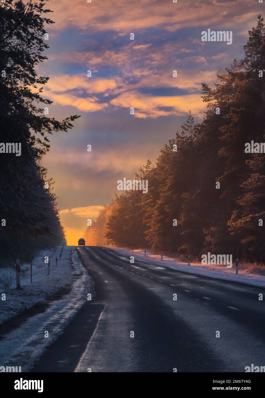 Silhouette d'une voiture qui roule sur une route asphaltée dans la neige de soleil d'hiver. Véhicule se déplaçant sur la distance jusqu'à un coucher de soleil froid Banque D'Images