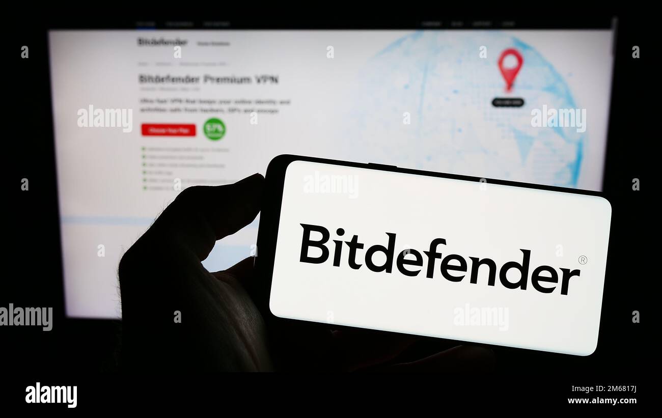 Personne tenant un téléphone portable avec le logo de la société roumaine de cybersécurité Bitdefender à l'écran en face de la page Web d'affaires. Mise au point sur l'affichage du téléphone. Banque D'Images