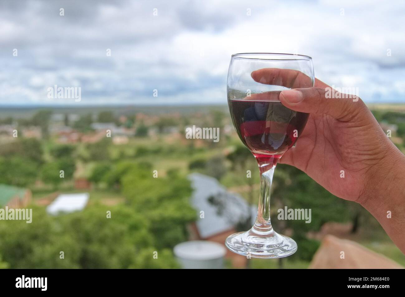 Verre de vin tenu sur la colline avec une vue magnifique sur le village s'étaler en dessous lors d'un été africain frais et couvert Banque D'Images