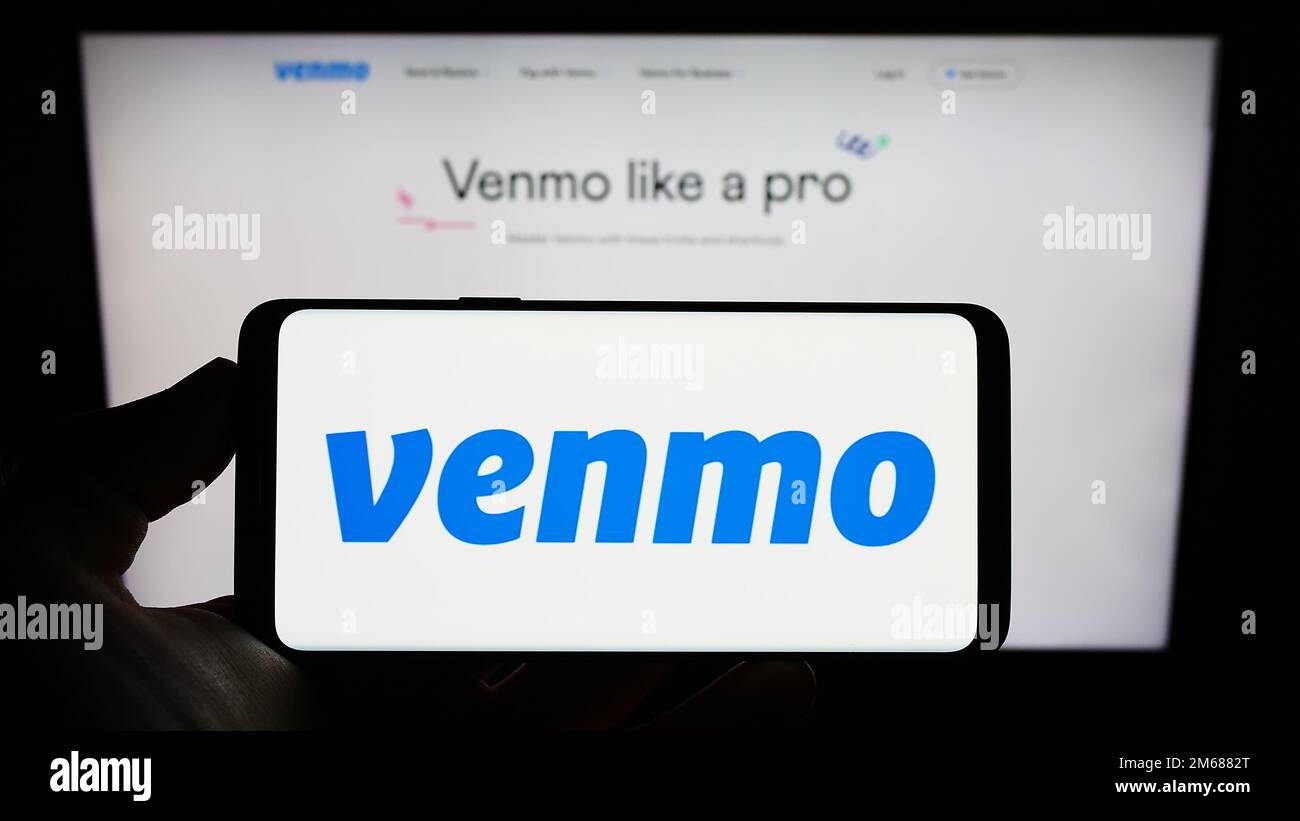 Personne tenant le téléphone portable avec le logo du service de paiement mobile Venmo à l'écran en face de la page web de l'entreprise. Mise au point sur l'affichage du téléphone. Banque D'Images