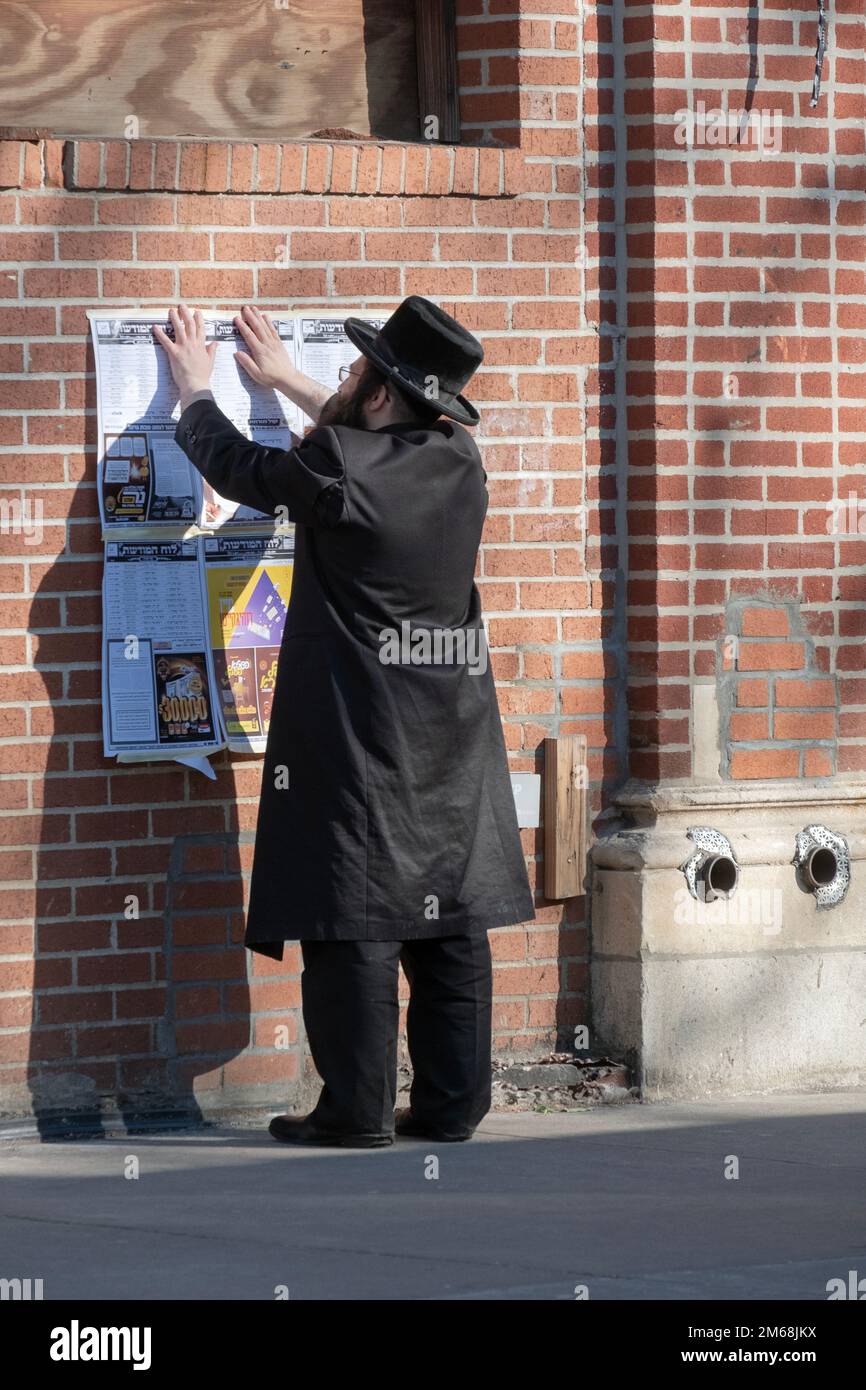 Un juif hassidique porte un panneau avec un calendrier d'événements religieux. Sur Lee Avenue à Williamsburg, Brooklyn, New York. Banque D'Images