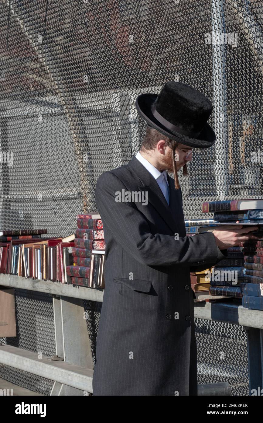 Un juif orthodoxe aux longs parures de curly se met à chercher des livres dans un magasin éclair en plein air sur un passage supérieur BQE à Brooklyn, New York Banque D'Images