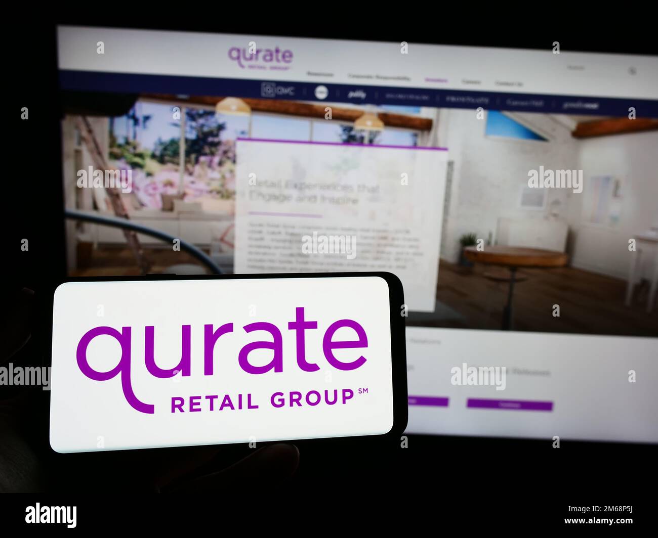 Personne tenant un smartphone avec le logo de la société de médias américaine Qurate Retail Inc. À l'écran devant le site Web. Mise au point sur l'affichage du téléphone. Banque D'Images