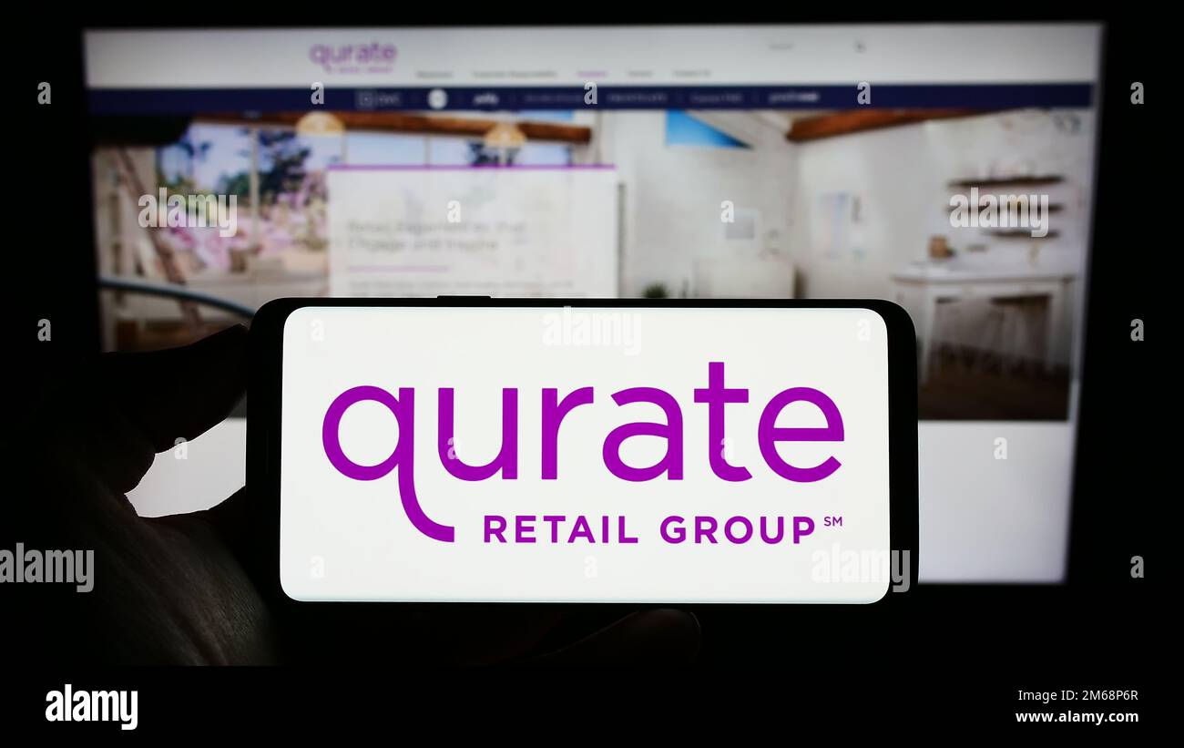 Personne tenant un téléphone cellulaire avec le logo de la société de médias américaine Qurate Retail Inc. À l'écran devant la page Web d'affaires. Mise au point sur l'affichage du téléphone. Banque D'Images