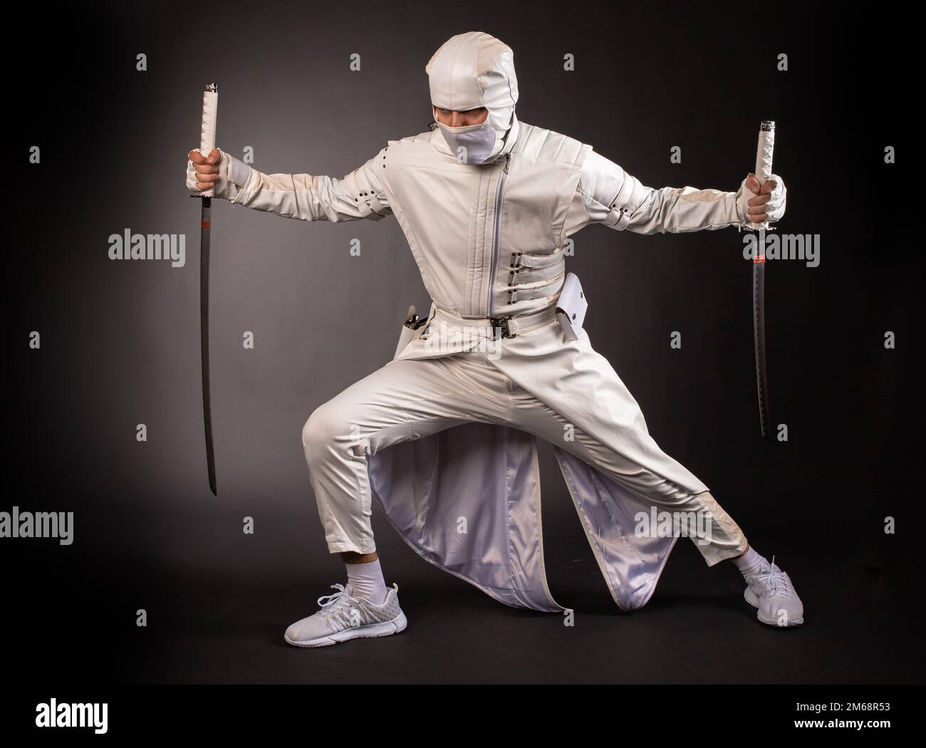 Un homme sous la forme d'un ninja de combat pose avec deux épées sur un fond noir Banque D'Images